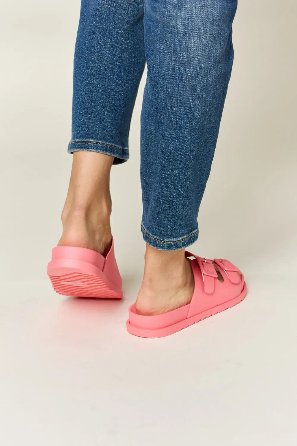 Woman wearing pink Legend Double Buckle Open Toe Sandals with blue jeans, showcasing the back view of the stylish footwear.