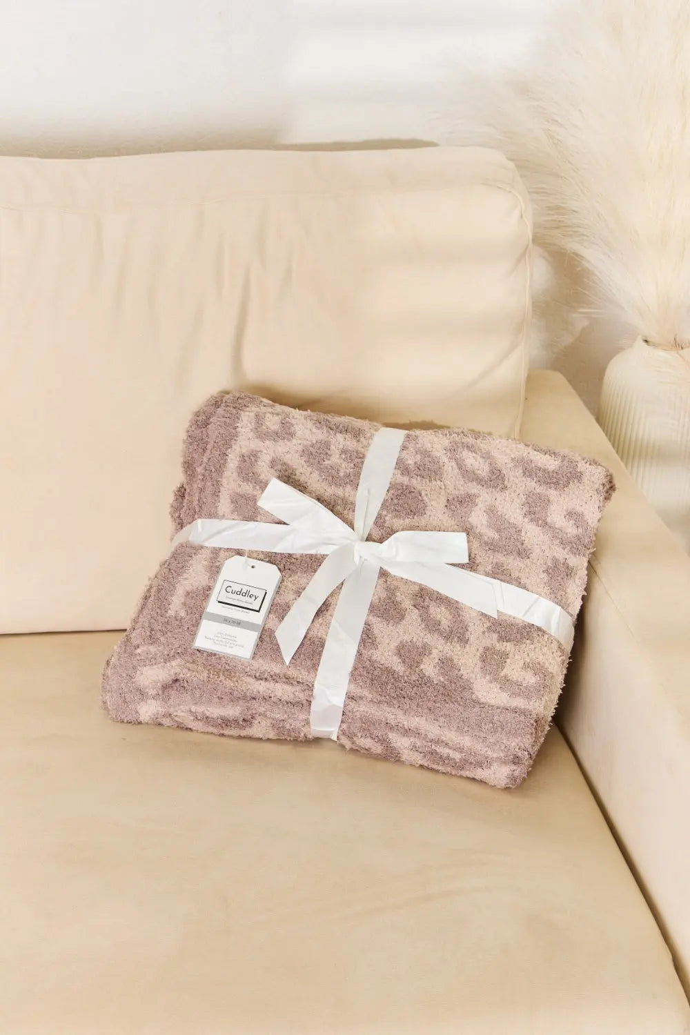 Cuddley Leopard Decorative Throw Blanket wrapped with a ribbon on a beige couch, adding a stylish touch to home decor.