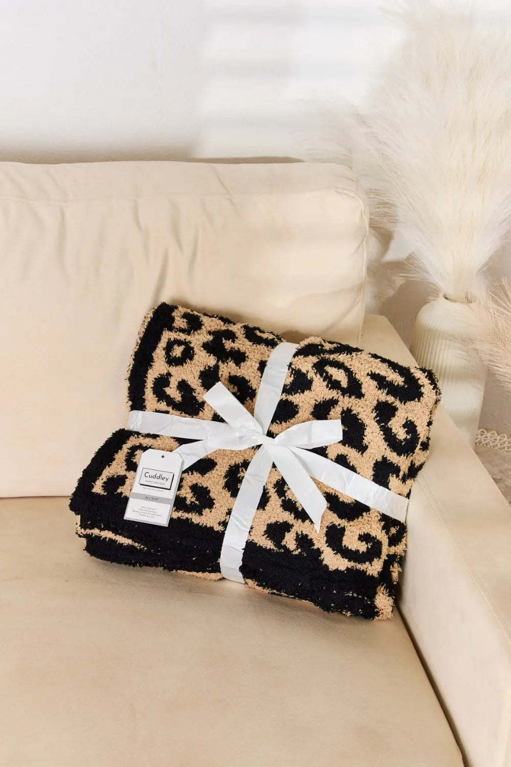 Cuddley Leopard Decorative Throw Blanket wrapped with a ribbon on a cream-colored sofa, adding stylish decor.