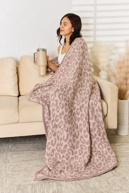 Woman wrapped in a Cuddley Leopard Decorative Throw Blanket on a sofa, enjoying a cozy moment.