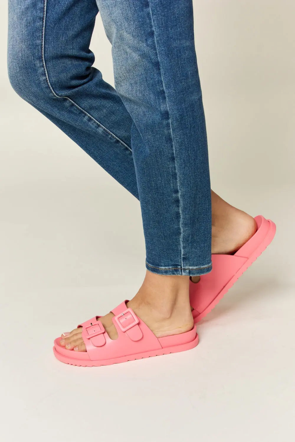 Woman wearing pink Legend Double Buckle Open Toe Sandals with denim jeans, showcasing stylish and comfortable footwear.